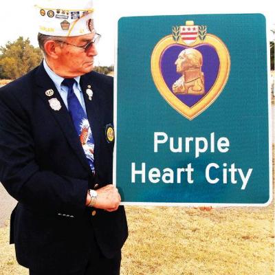 CDN | Robert S. Bryan City Councilman and U.S. Army veteran Bobby Stewart shows off one of the five signs proclaiming Clinton a Purple Heart City that will soon dot its primary entrances. Sacrifices of war dead will be noted here