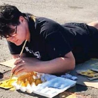 CHS student Ethan Maley uses stencils to paint numbers on parking spaces. Article Image Alt Text