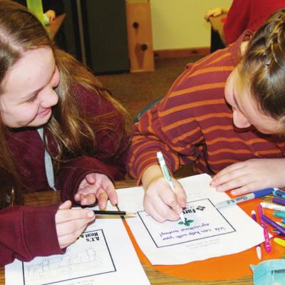 Hannah Cain, left, and Kate Stewart, both sixth graders at Western Oklahoma Christian School, work on a couple of Design An Ad forms. Even with school out, WOCS students excel in designing ads for local businesses