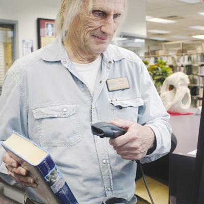 Paul Hierl, a librarian at Clinton Public Library, processes a newly returned book, ensuring it’s ready for the next patron to borrow. CDN | Staff photo Checking book