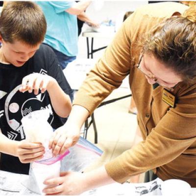 Logan Daley and Librarian Kathy Brunelle pour his finished homemade ice cream into a dish at Clinton Public Library. CDN | Caleb Blanchard Shaken, not stirred