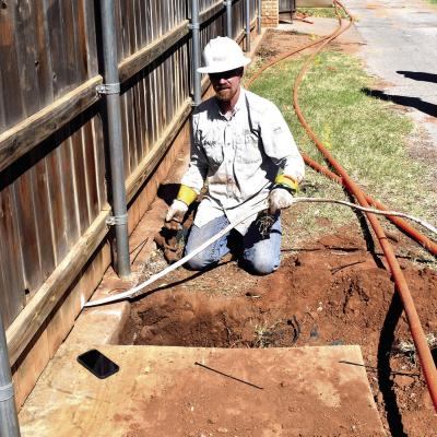 PSO worker Jeff Pinion works to install a new underground power line Tuesday that was bored through the day before by crews installing new internet service in the alley between Red Fork and Pond Ridge Road. Pinion is holding a temporary line that was inst Fiber optic projects lead to line breaks