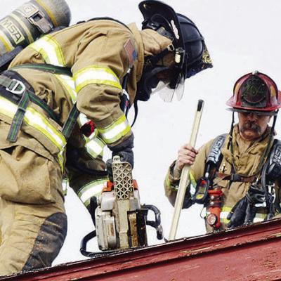 Clinton Firefighter Bobby Winans, left, uses a chainsaw to cut a hole in the roof of a closed building in the 2200 block of Modelle Avenue in a training exercise as Capt. Forrest Valentine looks on Tuesday afternoon. The property is scheduled to be demoli