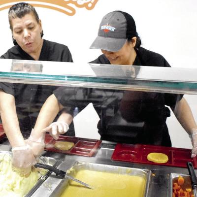 Southwest Elementary cafeteria employees Blanca Hernandez, left, and Magnolia Andablo prepare food for the day, similar to what the after-school meal program will look like at four Clinton Public Schools site. CDN | Emily Stephens After school meal program begins at CPS