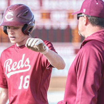 Harrison Crumley celebrates with first base coach Jeff King in a home game versus Kingfisher Monday. CDN | Adam Ewing Reds sweep seaso