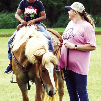 Eastside Academy student Kyi Williams, left, rides a horse while Sierra Ringer leads it along. CDN | Emily Stephens Horses, Eastside Academy kids come together for riding fun