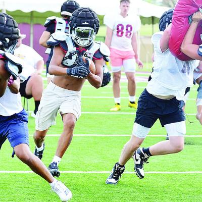 Clinton’s Jesus Gutierrez carries the ball between two blocks set by CJ Begay on DJ Lister, left, and Zaryk Baker on Vince Jones during preseason practice at the Tornado Bowl. CDN | Sam Goodwyn